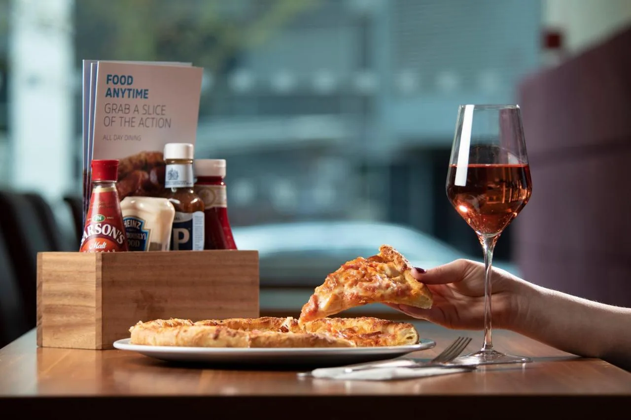 a person holding a slice of pizza and a glass of wine at Holiday Inn Express Cambridge by IHG in Cambridge